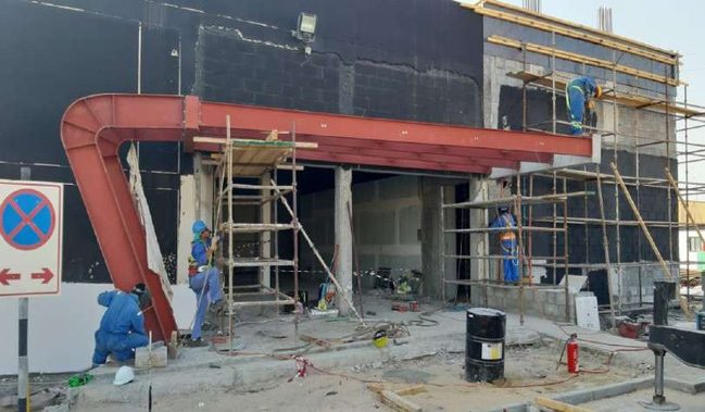 Curved red steel canopy under construction with scaffolding